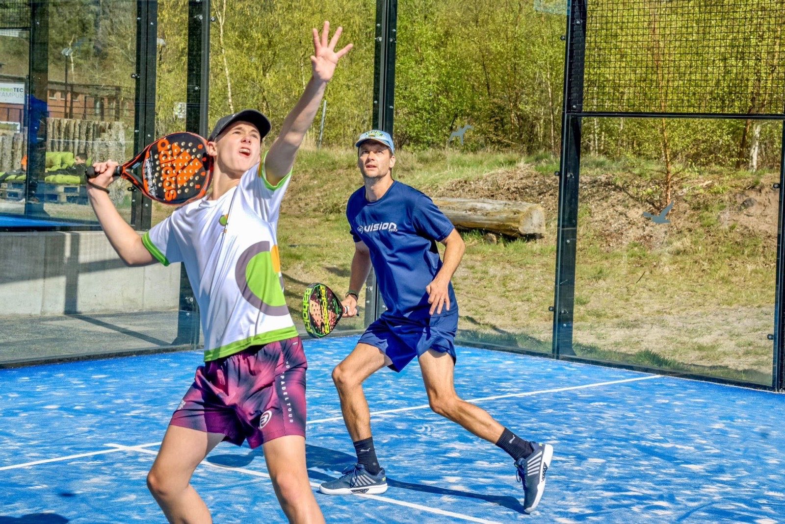 Spieler im Ballwechsel auf blauem Padelplatz